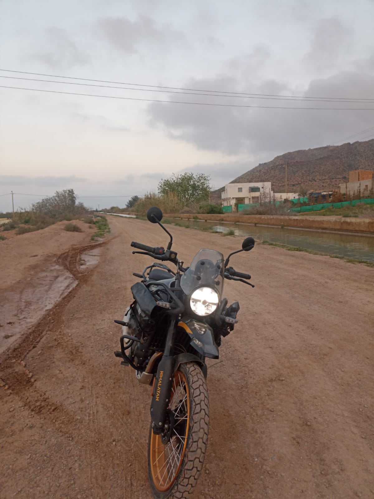 Zwarte Royal Enfield Himalayan adventure motorfiets op een stoffige onverharde weg langs een irrigatiekanaal