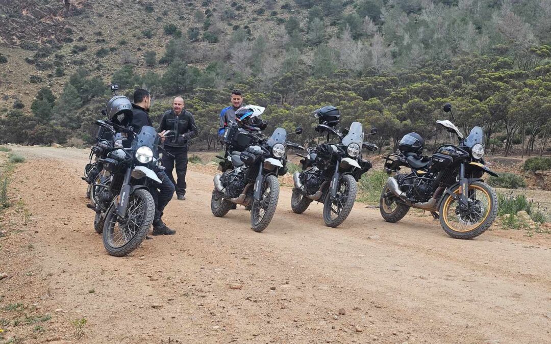 Drie motorrijders bij vier bepakte adventuremotoren op een onverharde weg
